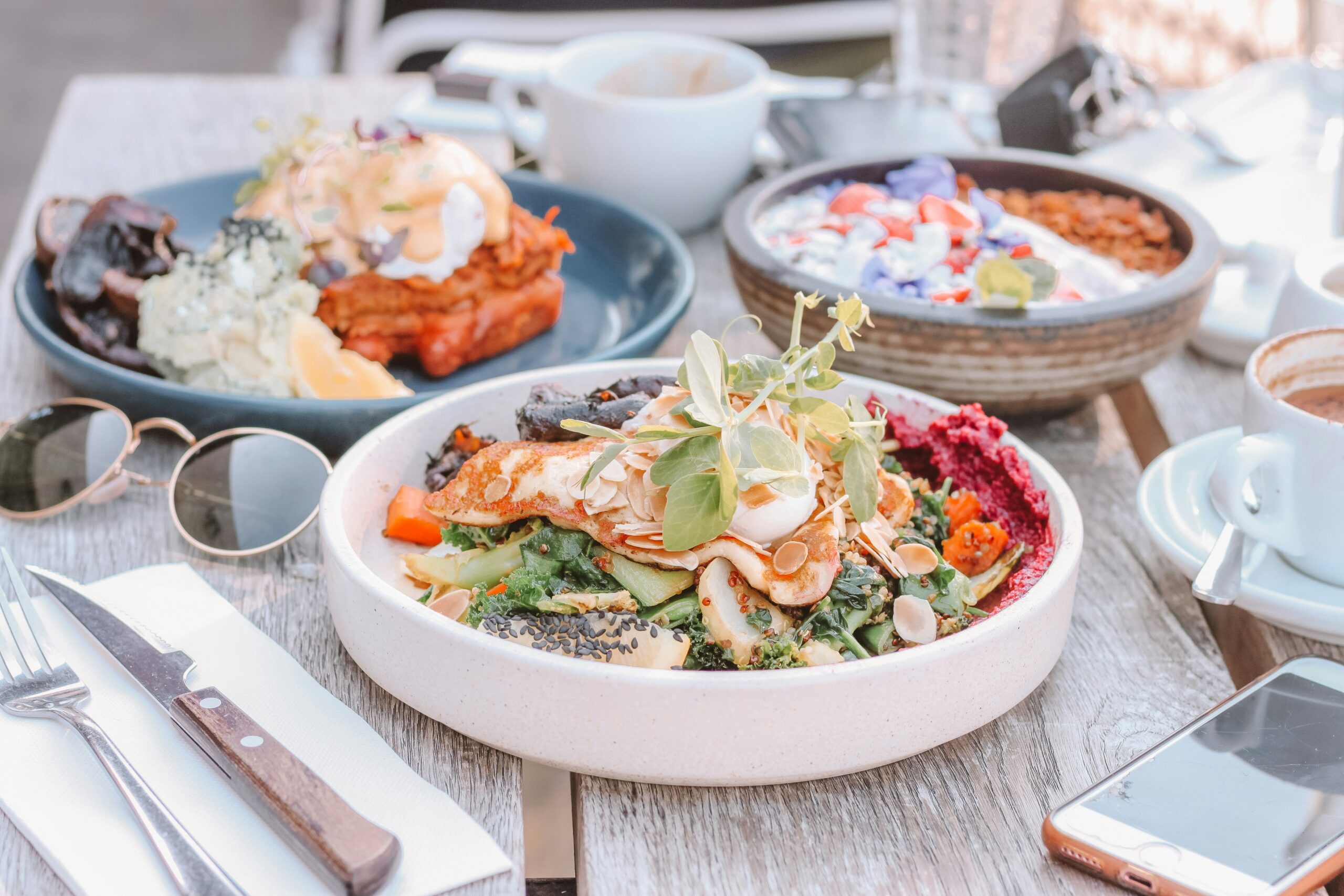 A beautifully arranged healthy breakfast featuring avocado toast with a poached egg, a bowl of fresh fruit, and a glass of orange juice on a wooden table.