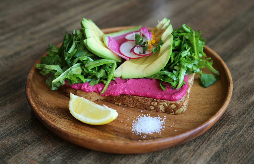 A slice of whole-grain toast topped with creamy avocado, vibrant beet hummus, and a sprinkle of seeds.