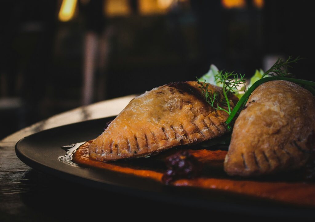 Golden, crispy veggie empanadas filled with a savory mix of vegetables, served with a side of dipping sauce.