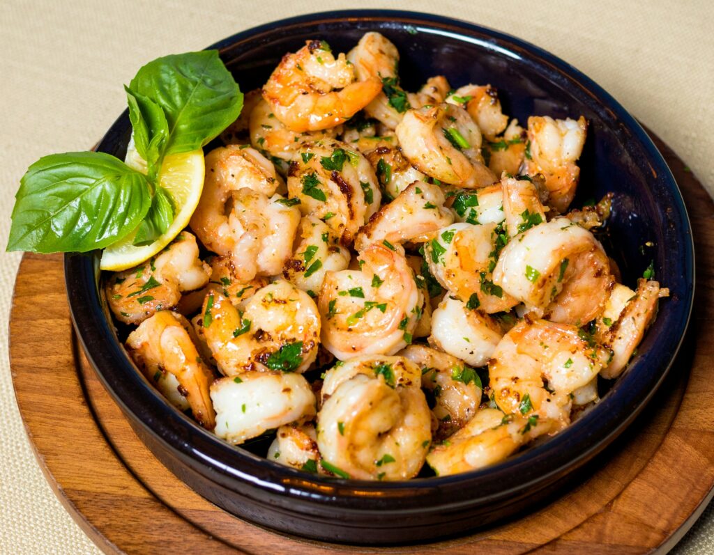 Garlic butter shrimp served in a black ceramic dish, garnished with fresh basil leaves and a lemon wedge, on a wooden serving board.