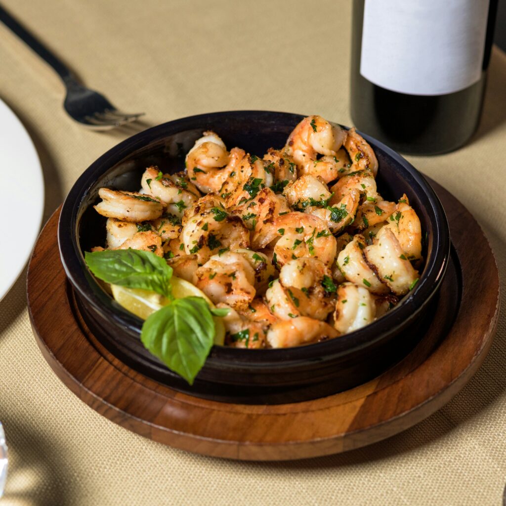 Garlic butter shrimp served in a black ceramic dish, garnished with fresh basil leaves and a lemon wedge, on a wooden serving board.