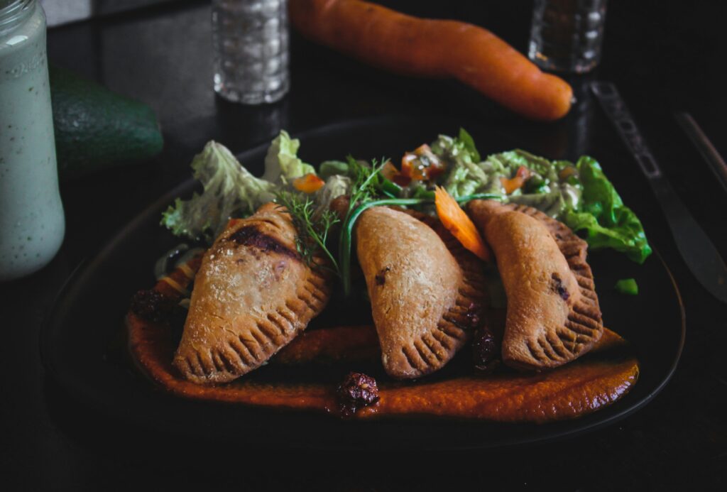 Golden, crispy veggie empanadas filled with a savory mix of vegetables, served with a side of dipping sauce.